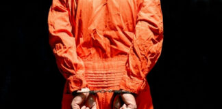 Person in orange jumpsuit handcuffed behind their back.