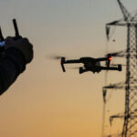 Hand operating drone near power lines at sunset.