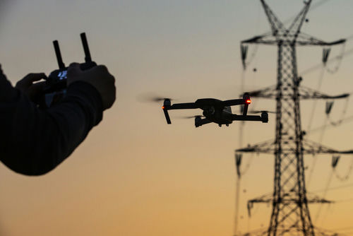 shutterstock_1827281051 Hand operating drone near power lines at sunset.