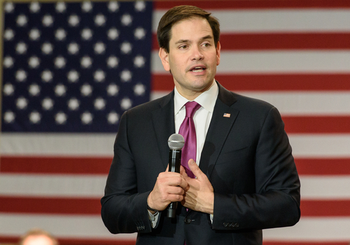 A politician speaking into a microphone in front of an American flag