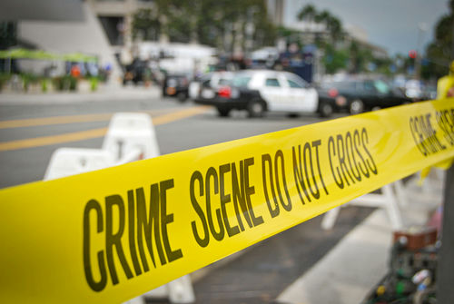 Crime scene tape cordoning off a street with police cars in the background