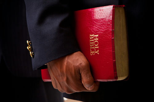 shutterstock503430328jpg Person in a suit holding a red Holy Bible