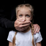 When Institutions Failed Those Most Vulnerable Man covering young girls mouth with hand.