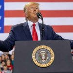 Person speaking at a podium with American flag backdrop.