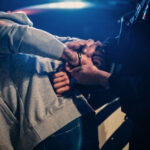 Person being handcuffed by an officer beside a police car at night