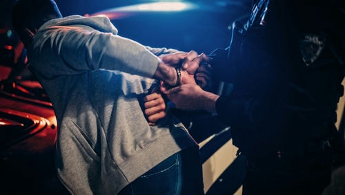 Person being handcuffed by an officer beside a police car at night