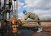 The Unbelievable Reason For Their Workforce Crisis Worker in blue hard hat operating rusty oil pump equipment outdoors