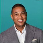 smiling man in gray suit against teal background