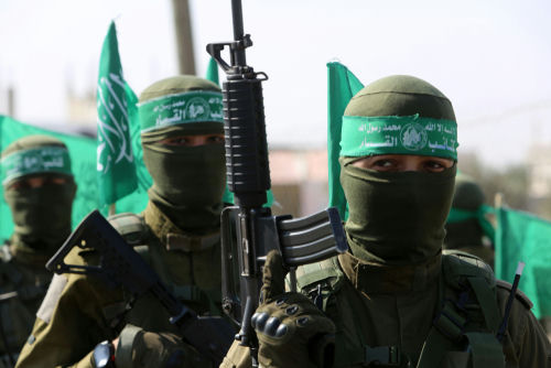 Militants in uniforms and masks holding green flags and guns.