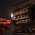 Power Prices EXPLODE — Blackouts Hit hand holding a lit match near an electrical breaker panel