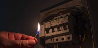 hand holding a lit match near an electrical breaker panel