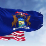 United States and Michigan flags waving against blue sky.