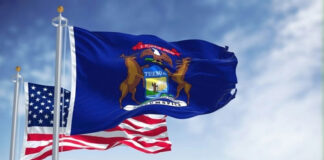 United States and Michigan flags waving against blue sky.