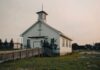 Small white church with steeple and cross at sunset