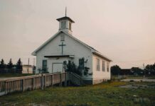 Small white church with steeple and cross at sunset