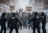 Protesters holding signs against ICE in a snowy urban setting