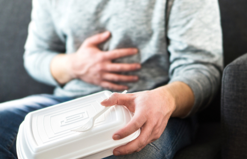 Person holding stomach with one hand, food container in other.