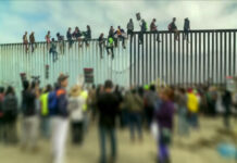 Crowd and people climbing large border wall during protest.