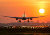 Airplane landing at sunset on illuminated runway.