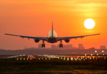 Airplane landing at sunset on illuminated runway.