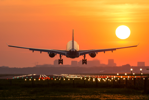 Airplane landing at sunset on illuminated runway.